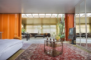 A hotel room with a bed, a glass coffee table with bottles, a sofa, and a television.