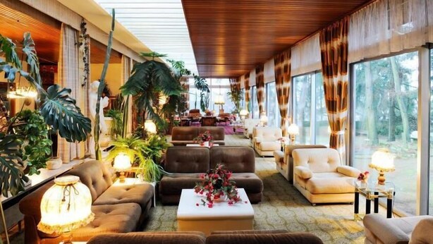 Amplia sala de estar con asientos cómodos, ventanas grandes y abundante vegetación de interior.