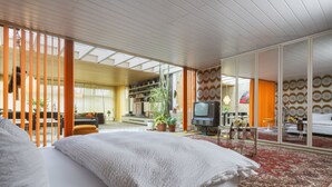 Un dormitorio amplio con una cama grande, televisión y una zona de comedor con cortinas naranjas.