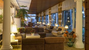 Un vestíbulo espacioso con varias zonas de estar, ventanas amplias y plantas decorativas.