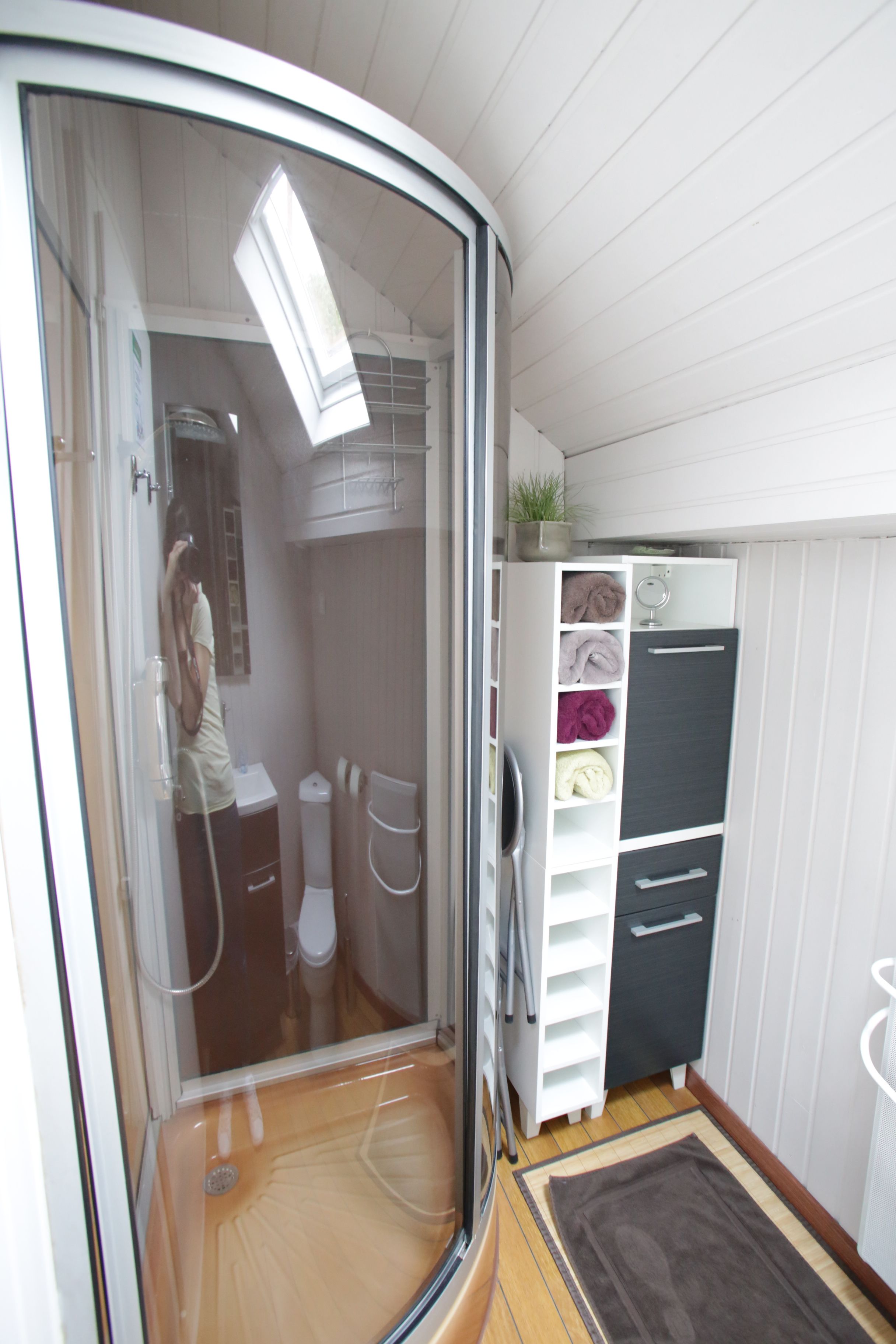 A compact bathroom with a shower, toilet, and storage unit.