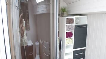 A compact bathroom with a shower, toilet, and storage unit.