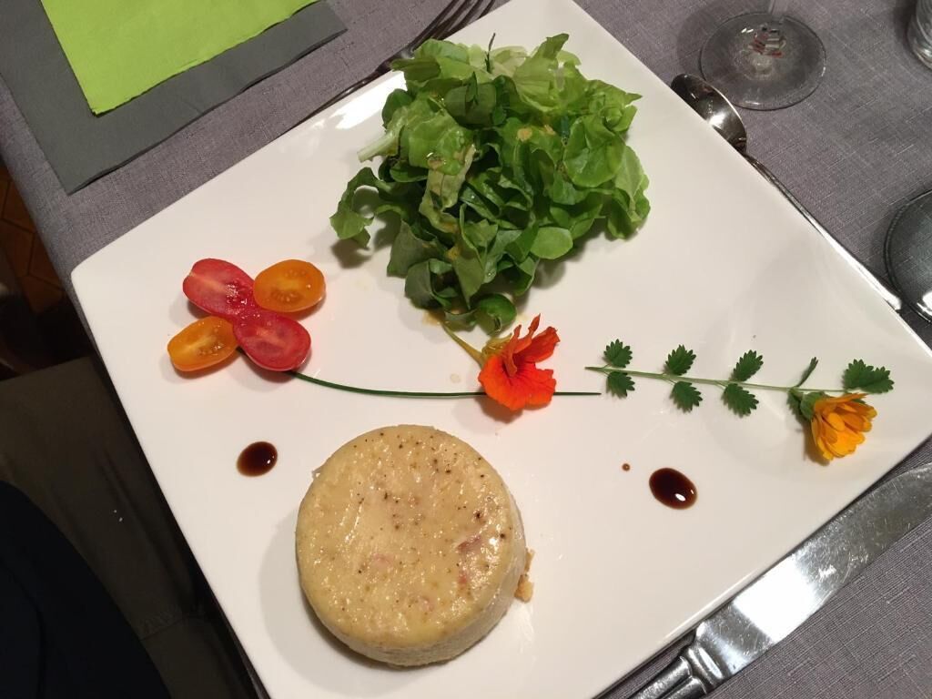 A plate with a round food item, a bunch of green leaves, and some red and yellow vegetables.