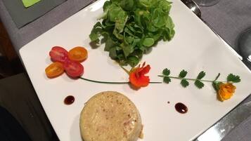 A plate with a round food item, a bunch of green leaves, and some red and yellow vegetables.