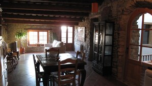 A rustic dining area with a stone wall, wooden furniture, and a large window providing natural light.
