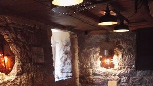 A long wooden table with menus, surrounded by black leather chairs, in a room with stone walls and hanging lights. - Hotel Restaurant Es Lämmche (Breuberg)
