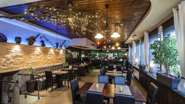 A restaurant with a curved ceiling, string lights, and a brick wall with guitars. Tables and chairs are arranged for dining. - Hotel Restaurant Es Lämmche (Breuberg)