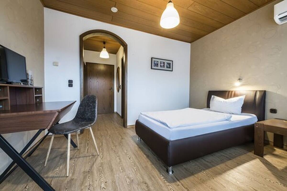 A modern hotel room with a wooden ceiling, a bed with white bedding, a desk with a chair, and a television.