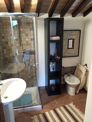 A bathroom with a glass shower enclosure, a sink, a bidet, and a black shelving unit with decorative items. - Agriturismo Cailuca (Pietralunga)