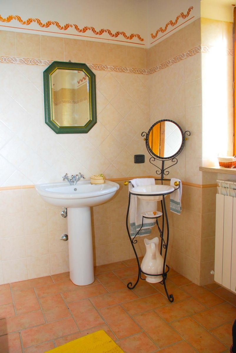 A bathroom with a pedestal sink, a wall-mounted mirror, and a radiator.