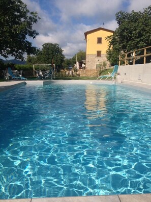 A clear swimming pool with blue water, surrounded by a wooden fence and trees. - Agriturismo Cailuca (Pietralunga)
