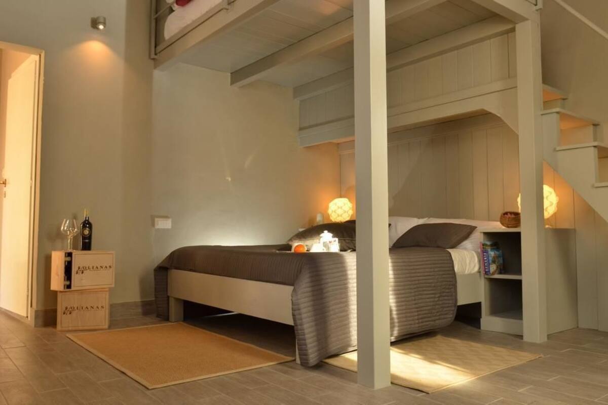 Un dormitorio con cama, mesita de noche y tocador. Tiene un cabecero de madera, un pequeño estante con libros y un estante fijado a la pared con una cesta.