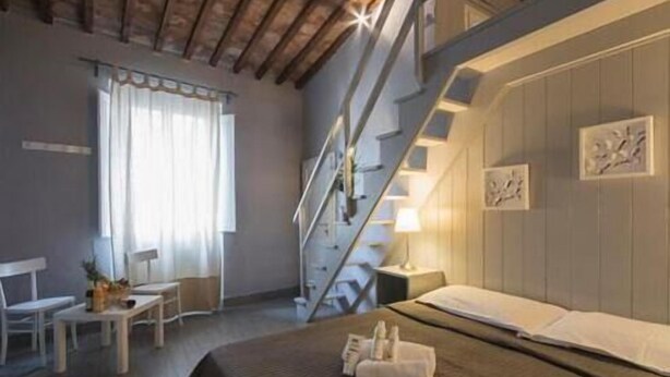 A hotel room with a bed, a desk, a chair, a staircase, and artwork on the walls. - B&B Le Casine di Firenze (Florence)