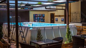 An outdoor swimming pool area with a covered patio, wicker furniture, and a small indoor bar area with framed pictures.