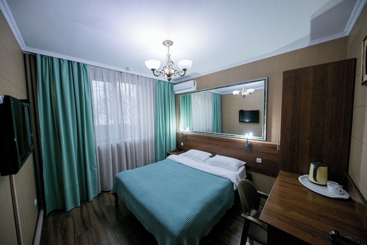 Una habitación de hotel con una cama, un escritorio, una silla, un espejo y una araña.