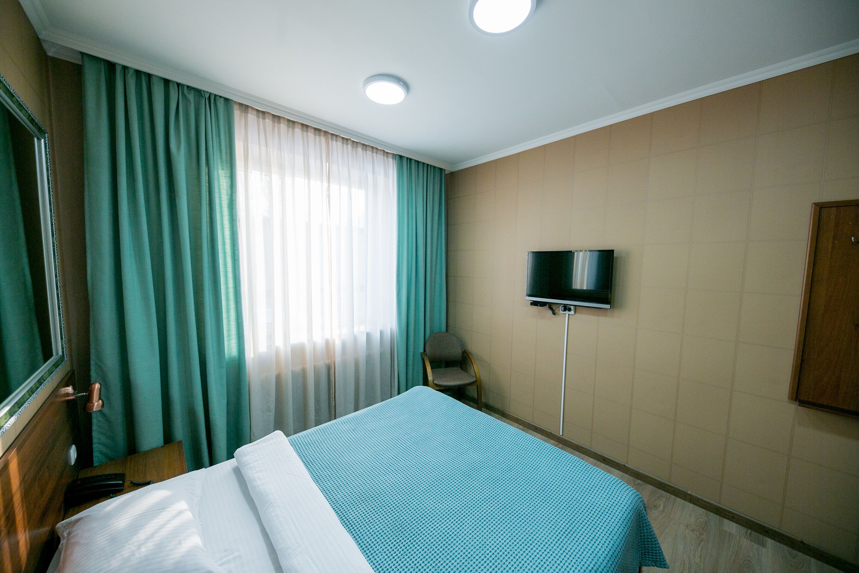 Een hotelkamer met een bed, gordijnen, een televisie en een stoel.
