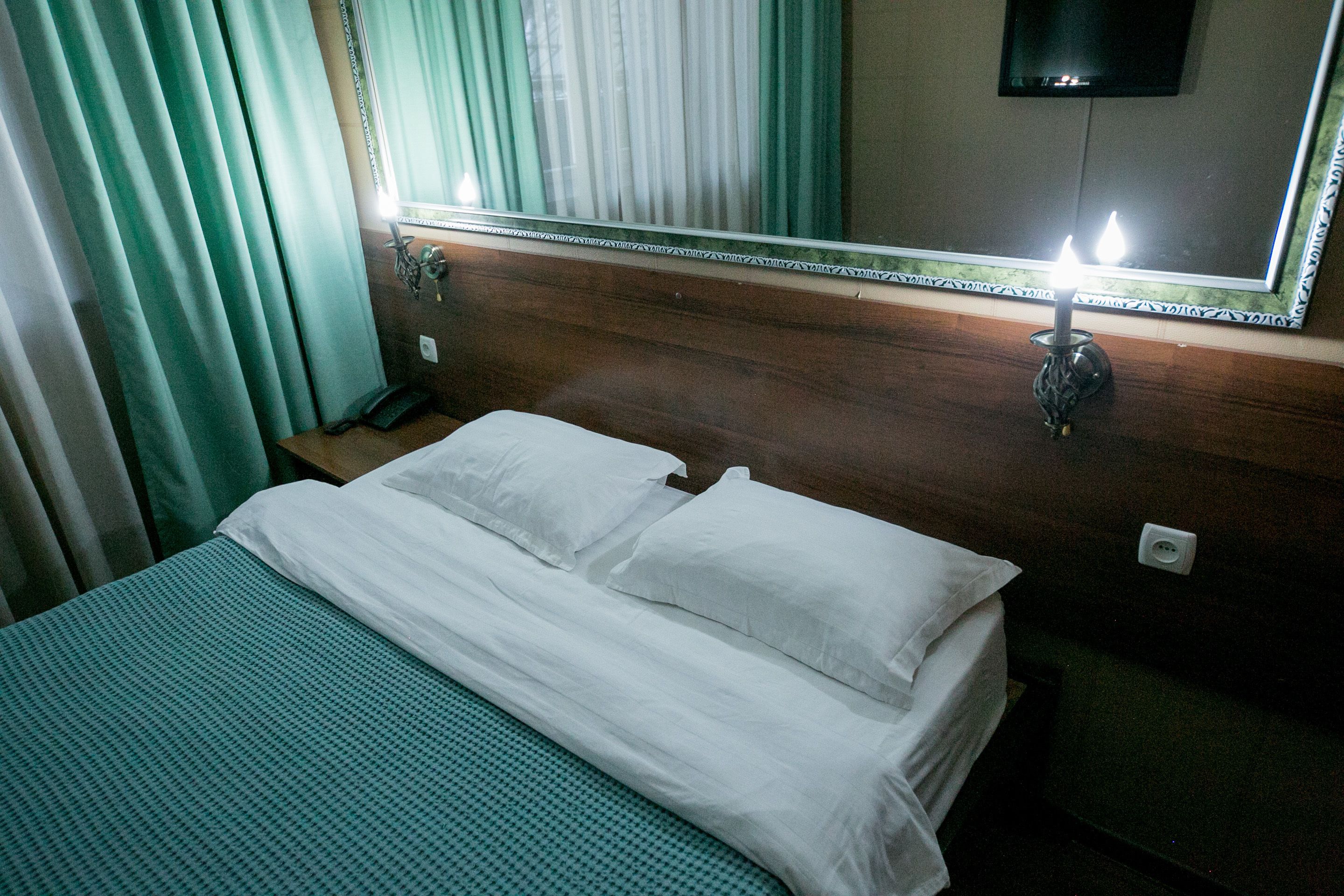 Una habitación de hotel con una cama, una mesita de noche, un espejo y un televisor montado en la pared.