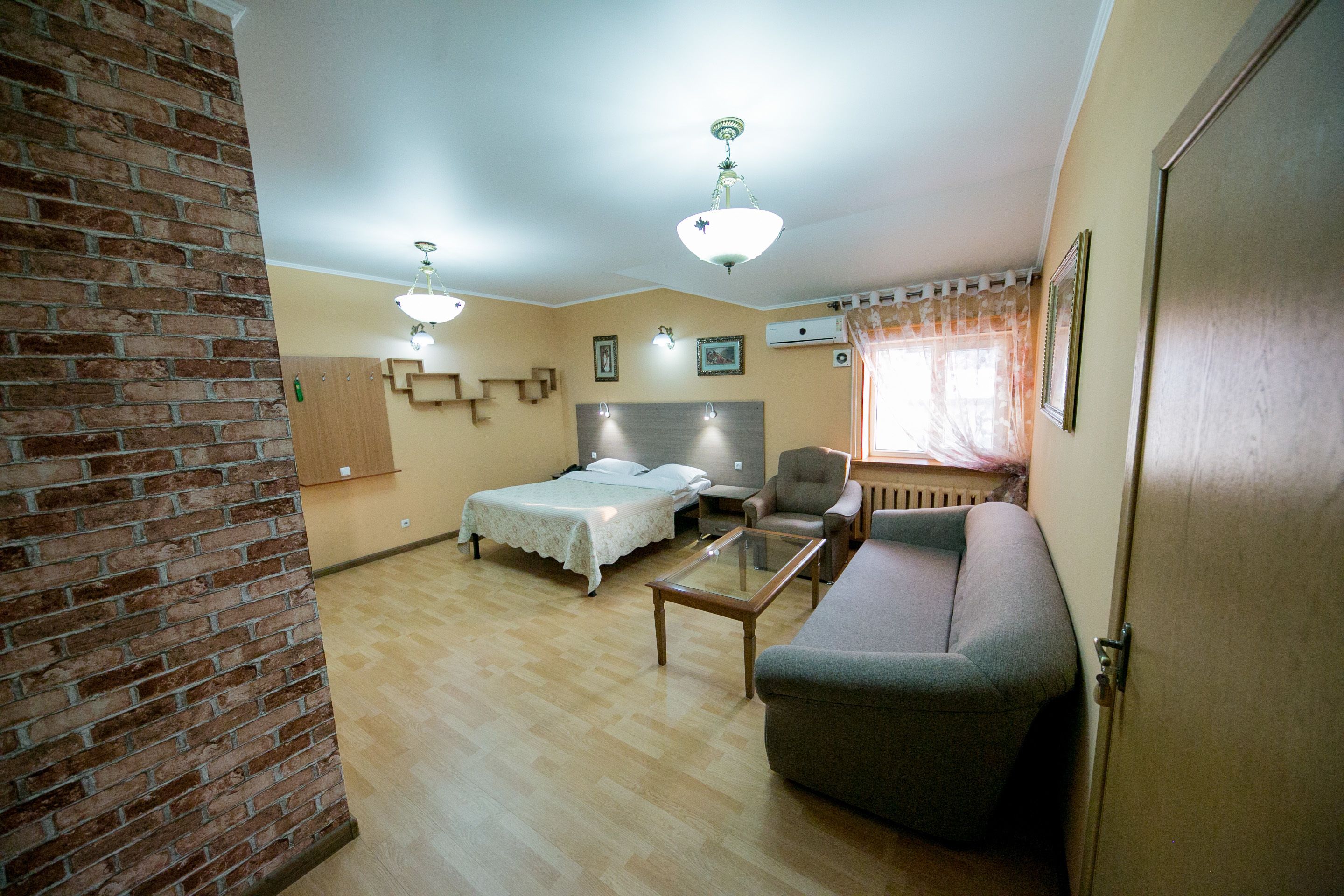 Una habitación con una pared de acento de ladrillo, una cama, un sofá, una mesa de centro de vidrio y una lámpara en el techo.
