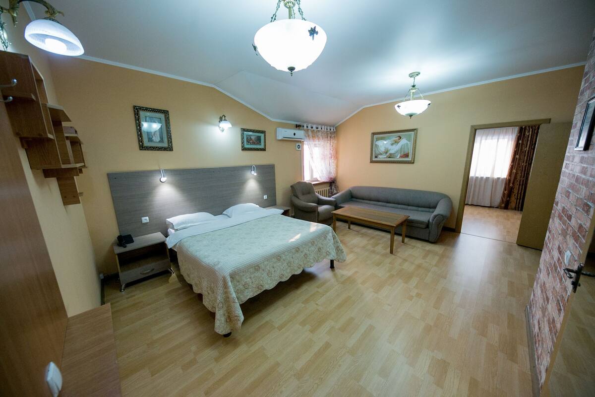 Un dormitorio con cama, sofá, mesa de centro y una silla. Se ve una escalera a la izquierda y una puerta a la derecha.