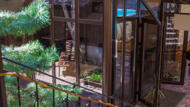 A glass-enclosed balcony with a metal railing, a potted plant, and a view of a brick patio and a pool.