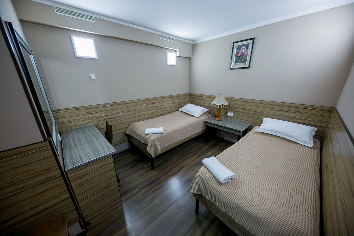 Una habitación de hotel con dos camas individuales, una mesita con una lámpara y un armario de madera.