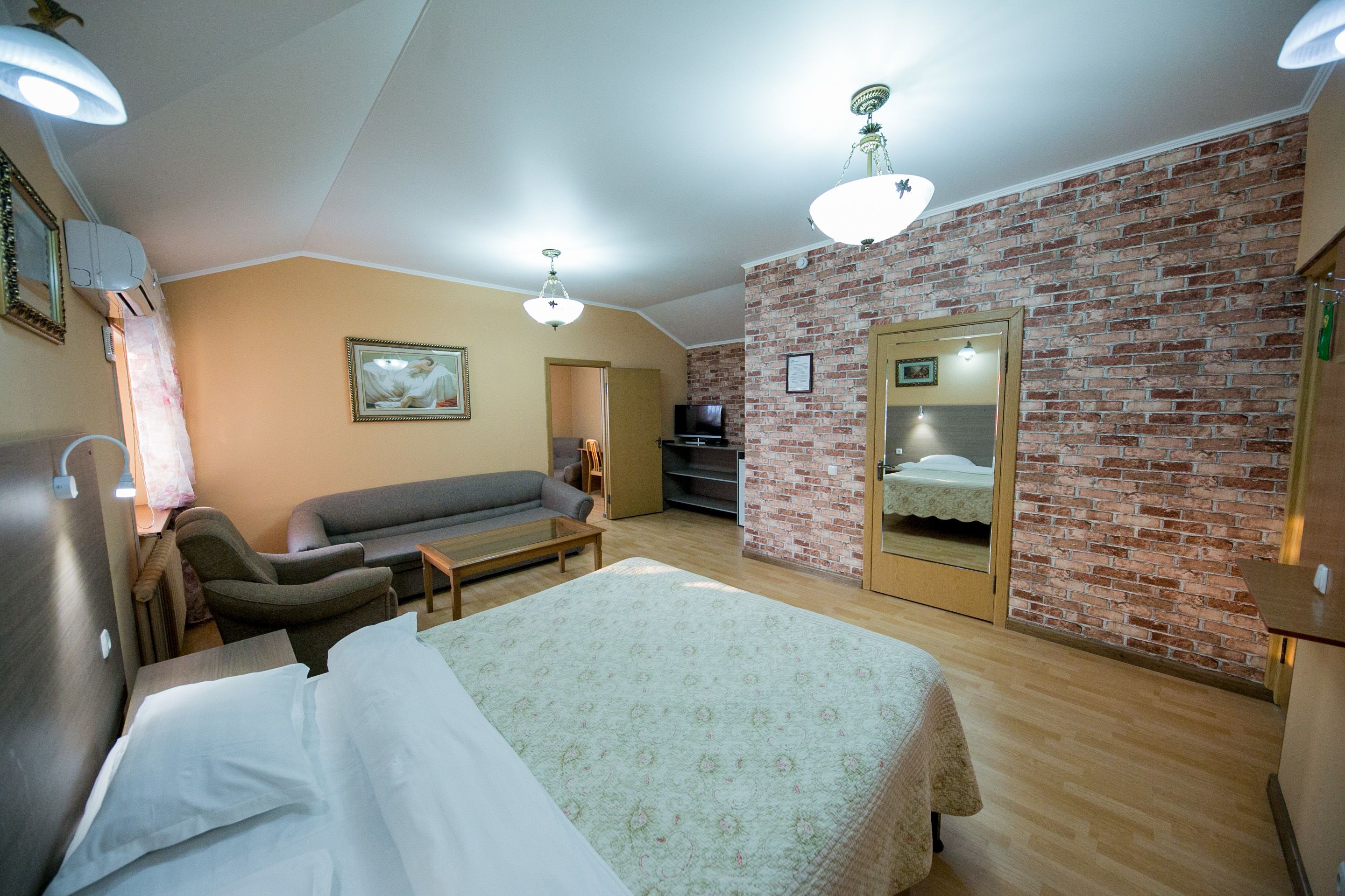 A hotel room with a bed, a sofa, a TV, and a brick wall.