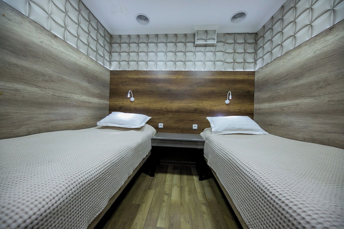 A room with two beds, a wooden headboard, and a small shelf.