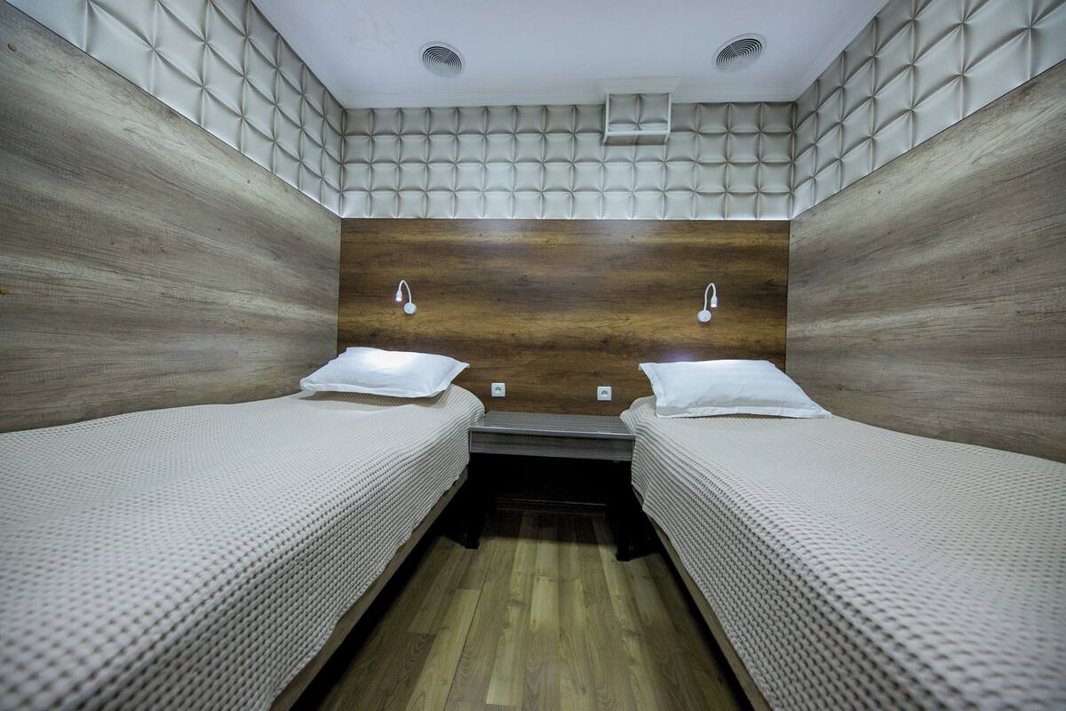 Una habitación con dos camas, cabecero de madera y una pequeña estantería.