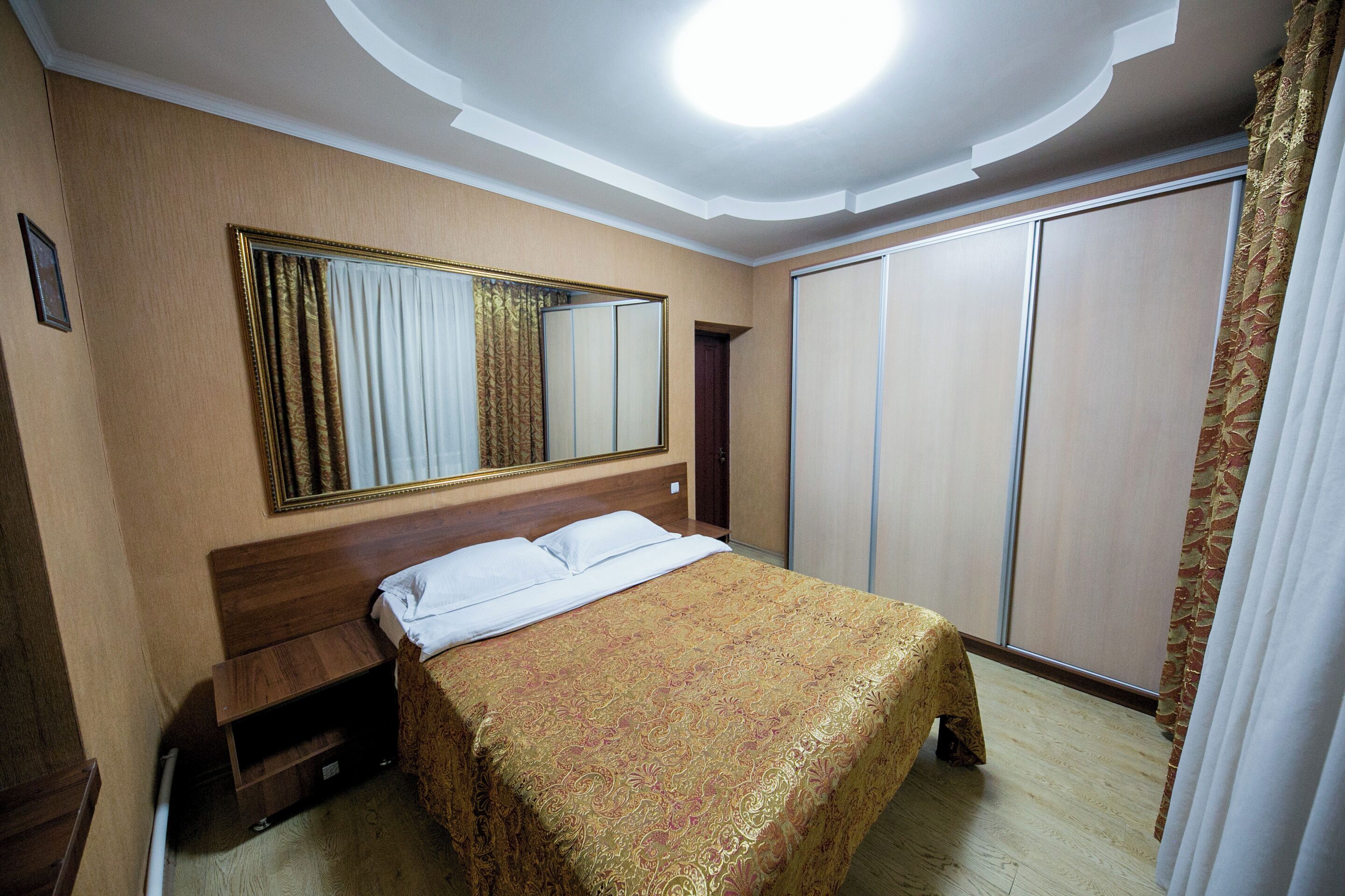 Habitación de hotel con cama, mesita de noche, espejo, armario y una lámpara en el techo.