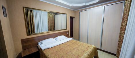 Habitación de hotel con cama, mesita de noche, espejo, armario y una lámpara en el techo.