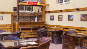 An outdoor seating area with wicker chairs and tables, a fish bar sign, and framed pictures on the wall.