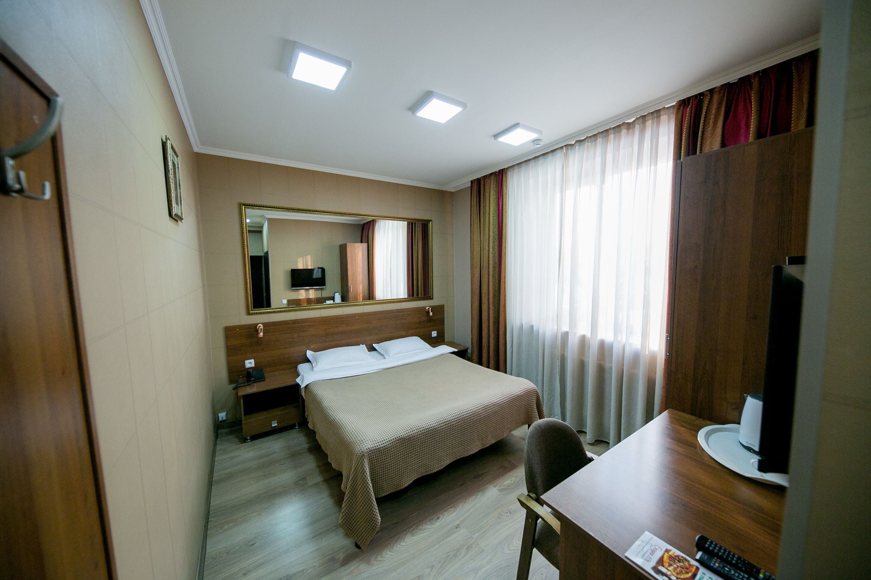 A hotel room with a bed, a desk, a chair, a television, and a mirror.