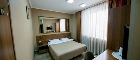 A hotel room with a bed, a desk, a chair, a television, and a mirror.