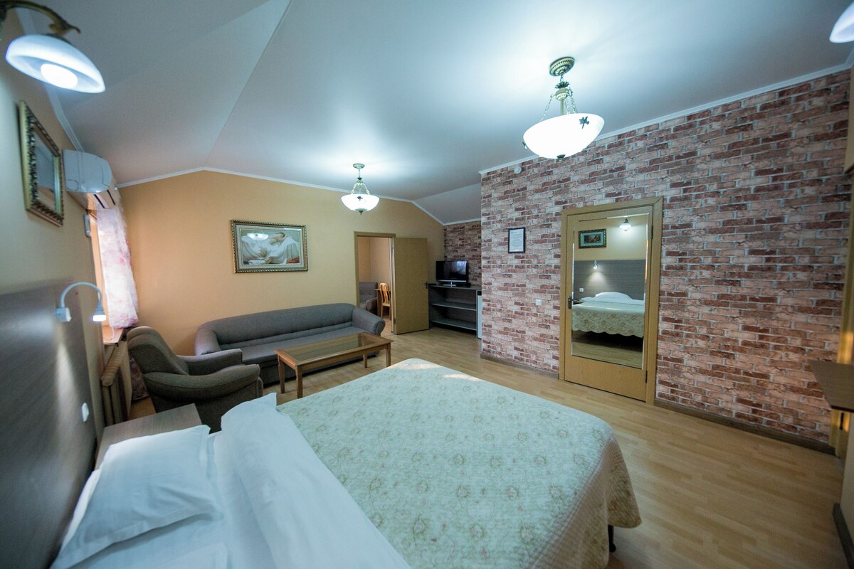 A room with a bed, a sofa, a television, and a brick wall.