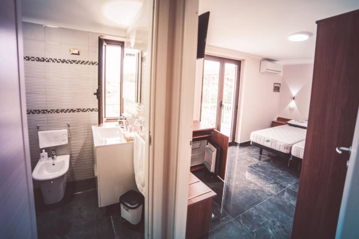 A compact hotel room with a bathroom, a small desk, a bed, and a window.