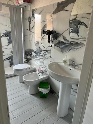 A bathroom with a toilet, bidet, sink, and a hairdryer mounted on the wall. - La Casa di Chiaretta (Falerna)