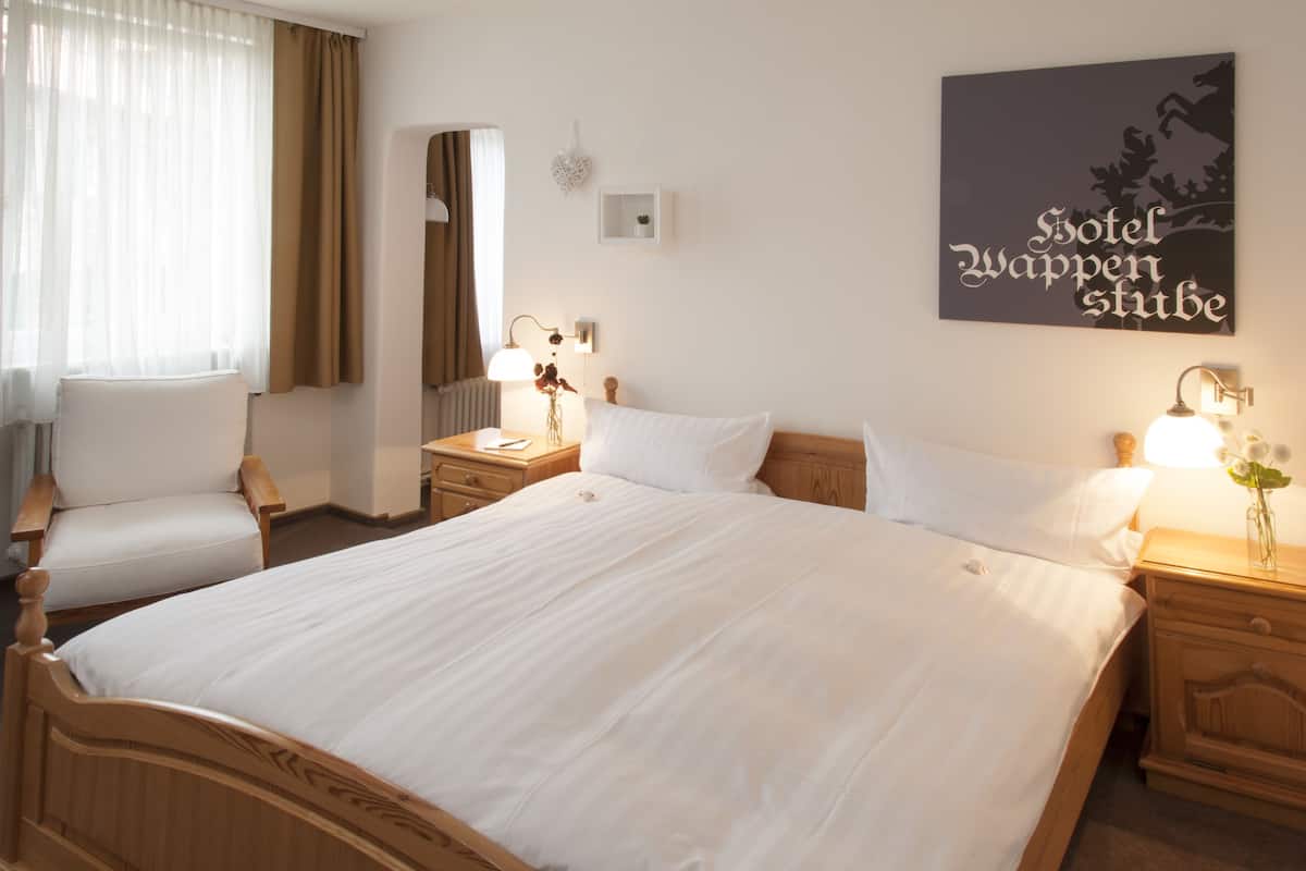A hotel room with a large bed, two bedside tables with lamps, a chair, and a wall-mounted artwork.