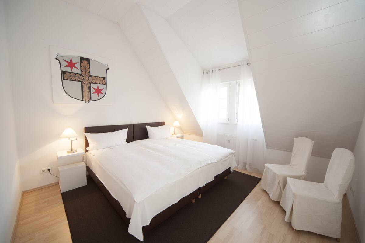 A bedroom with a bed, two bedside tables with lamps, a chair, and a coat rack.