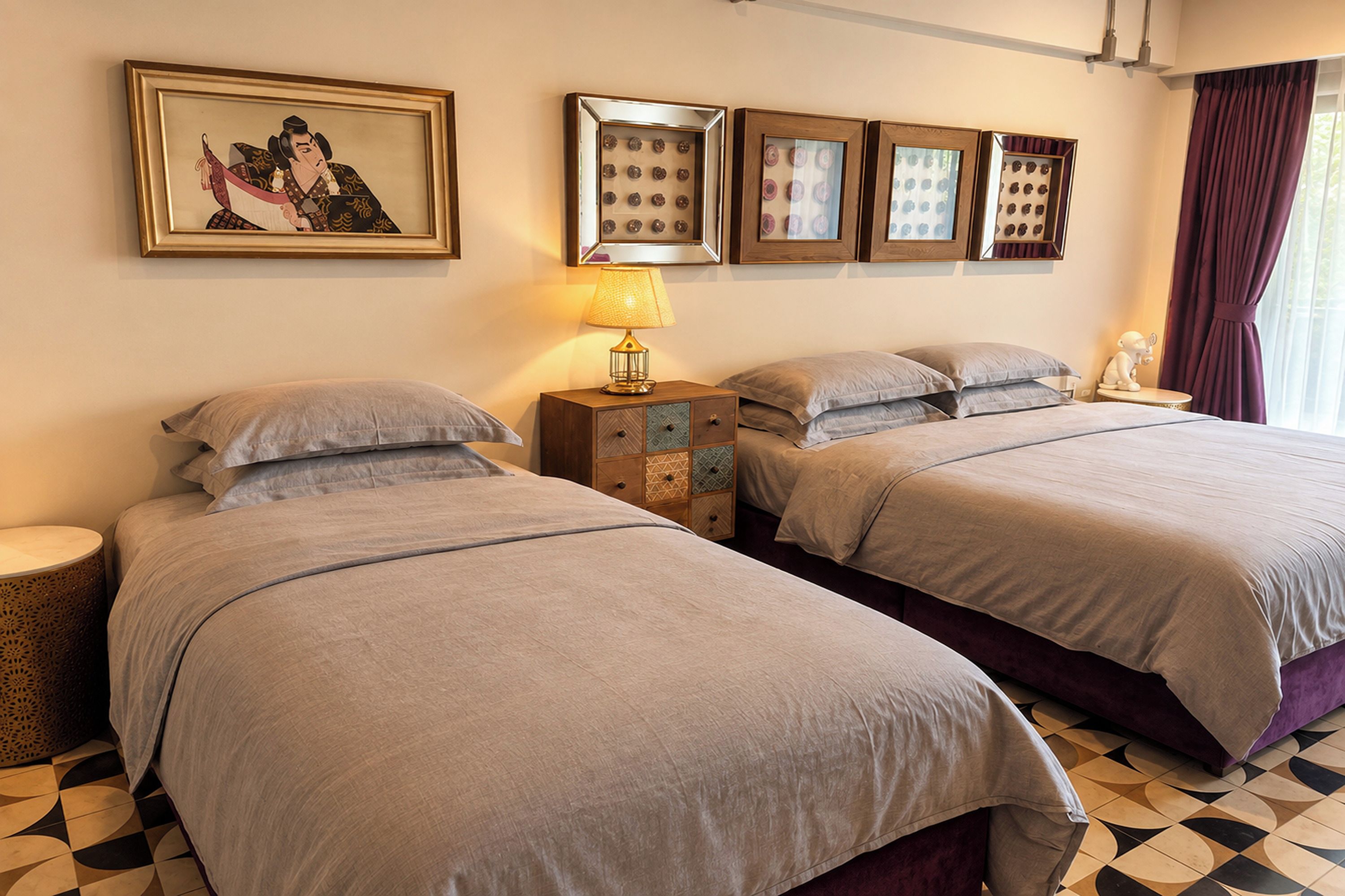 A hotel room with two beds, a nightstand, a lamp, and framed pictures on the wall.