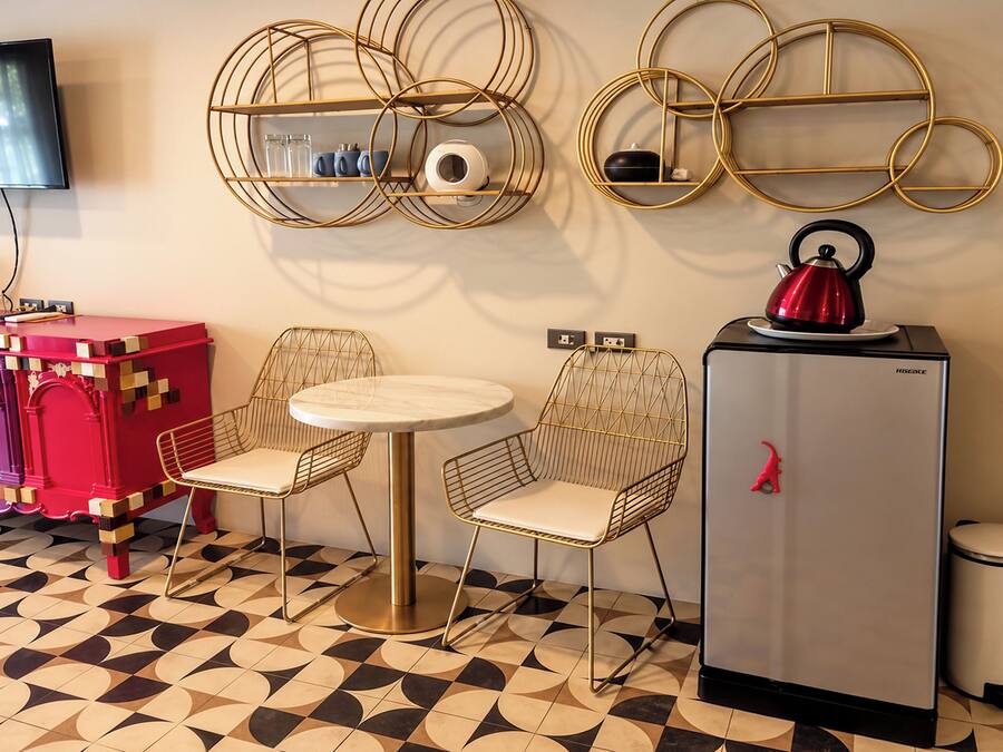 A compact kitchenette with a refrigerator, a kettle, and a small table with chairs.
