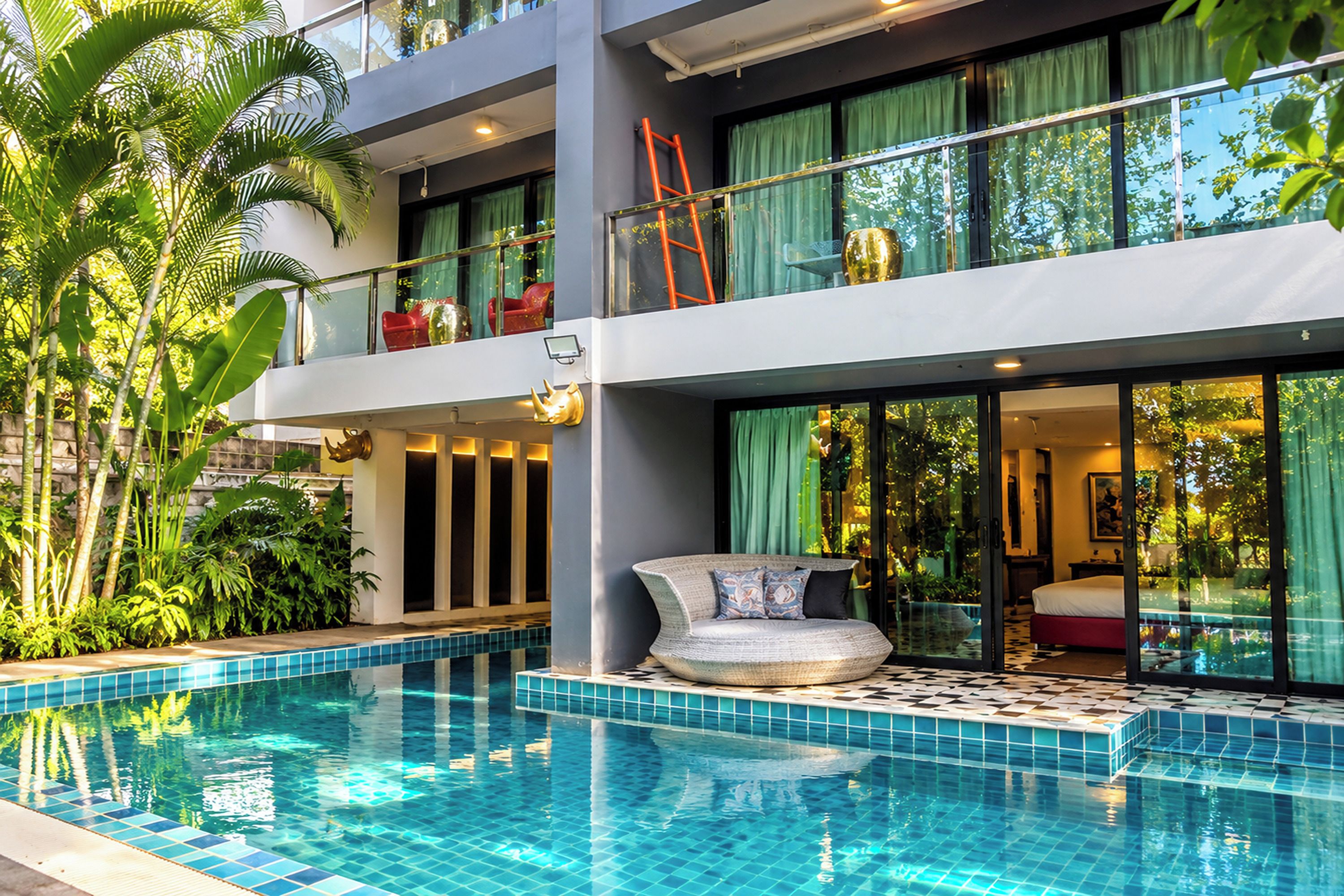 Un hotel moderno con piscina, mobiliario exterior y abundante vegetación.