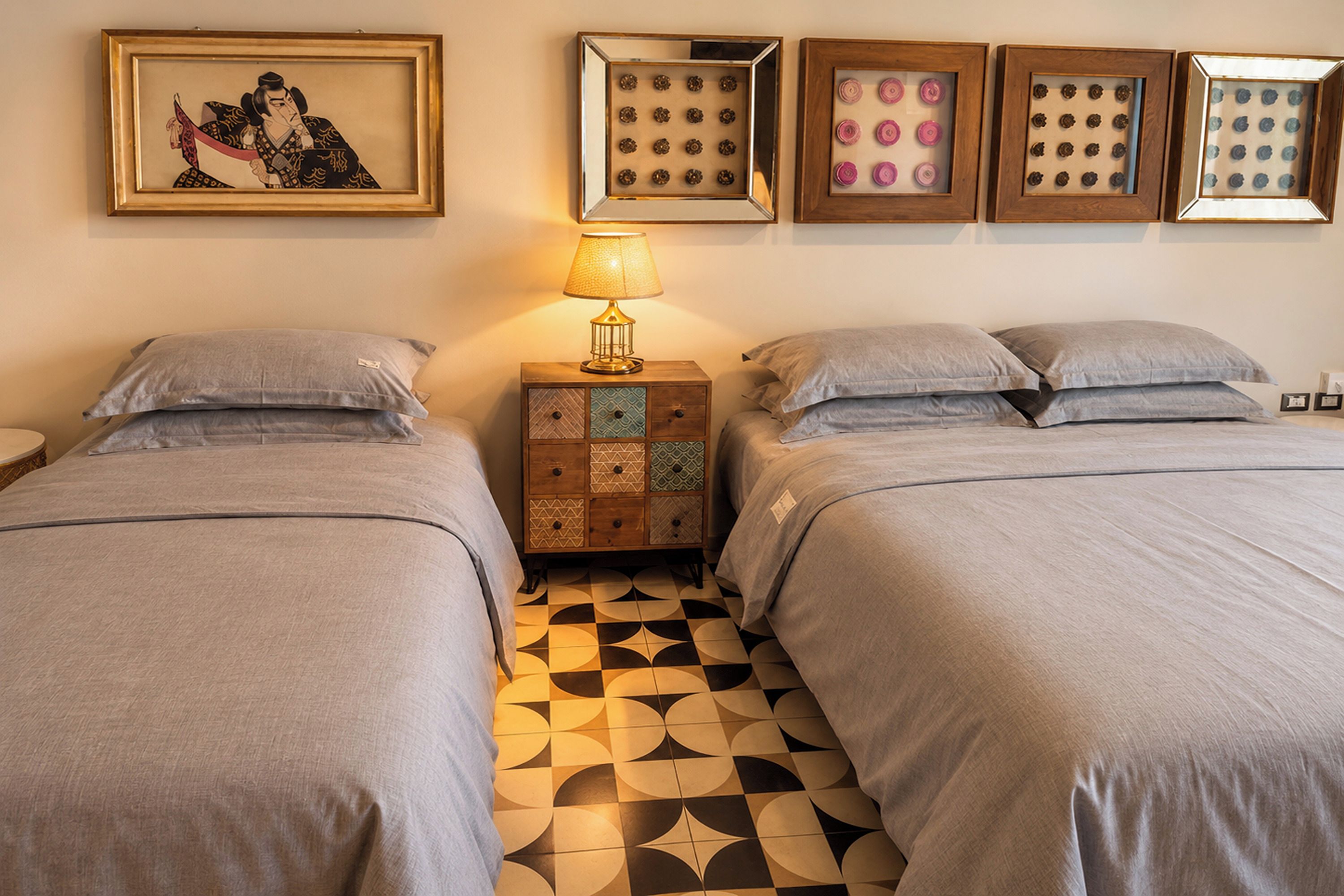 Una habitación de hotel con dos camas, una mesita de noche, una lámpara y cuatro cuadros en la pared.