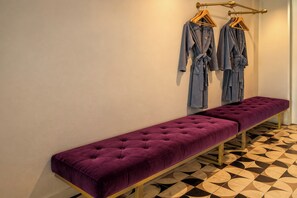 A bench with a tufted cushion, a clothing rack with hangers, and a patterned floor. - River Art Hotel (Chiang Mai)