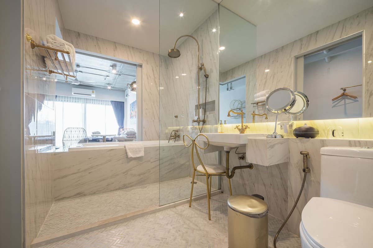 Une salle de bain moderne avec une douche à l’italienne en verre, un meuble-lavabo doré et des toilettes blanches.