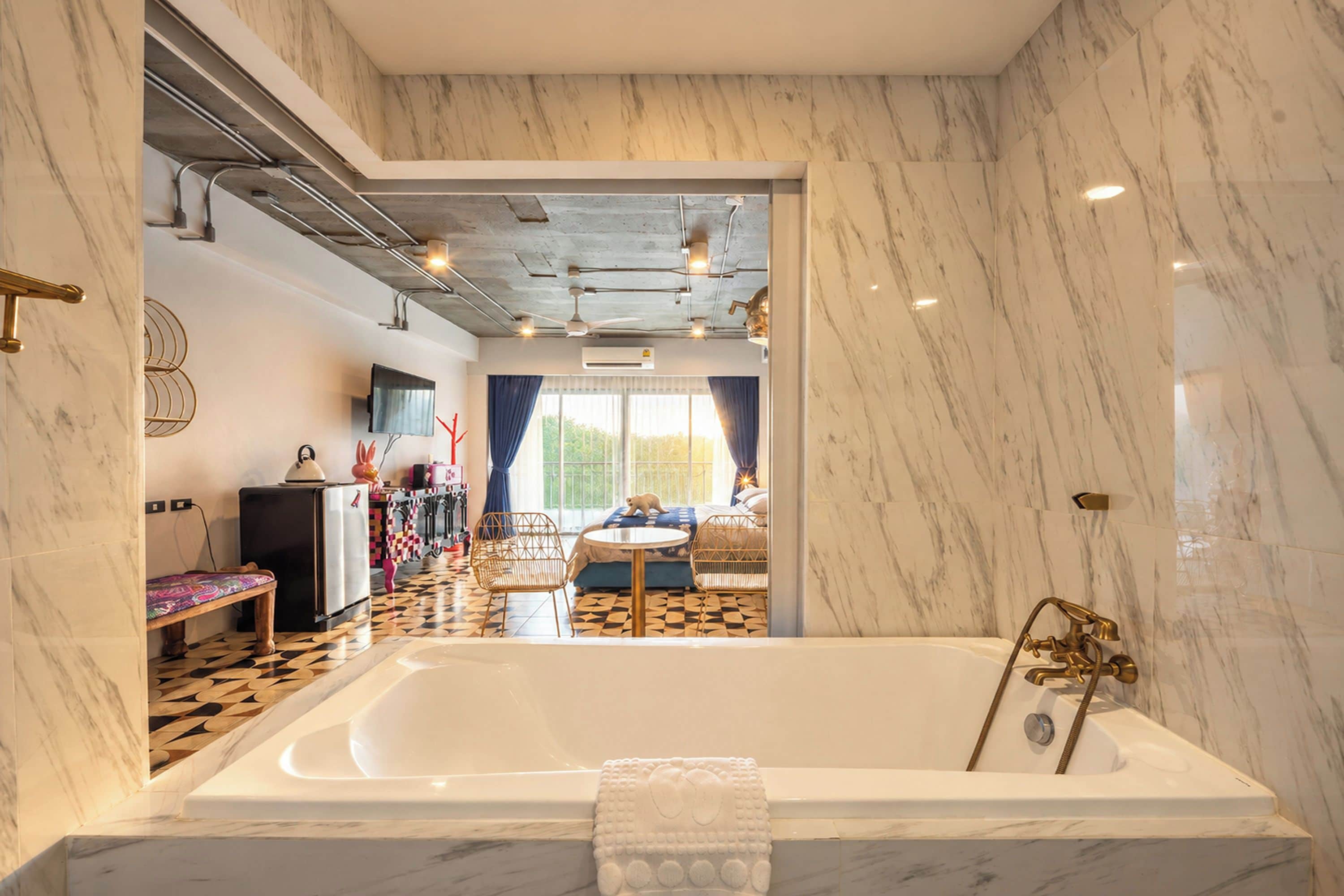 Ein modernes Badezimmer mit einer großen Badewanne, Marmorwänden und Blick in einen Wohnbereich mit Sofa und Esstisch.