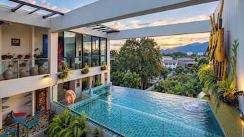 A modern hotel with a rooftop infinity pool, glass railings, and a view of the mountains.