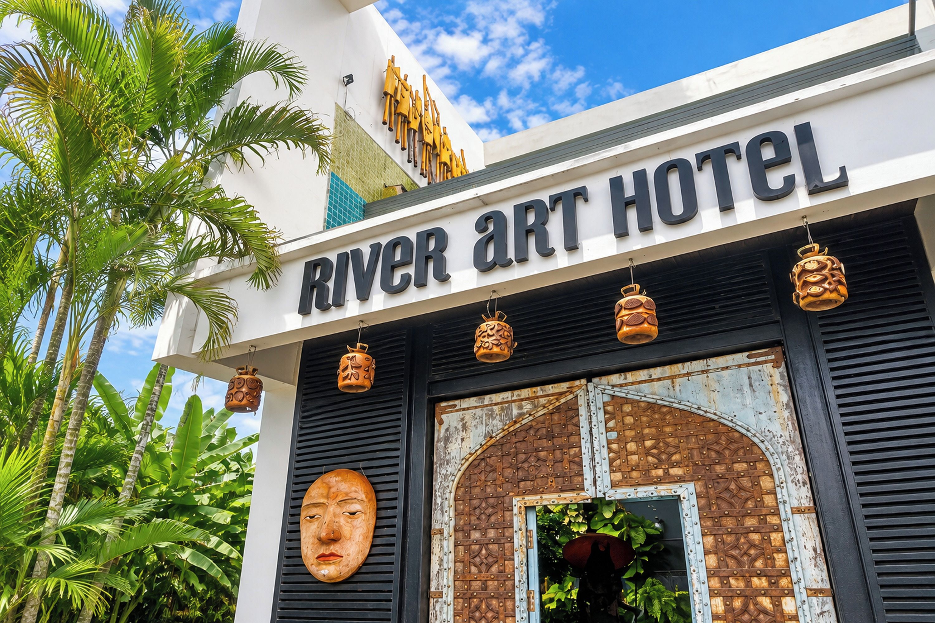The exterior of the River Art Hotel with a sign, decorative lanterns, and a large wooden door.