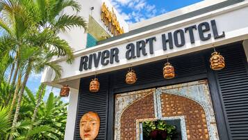 The exterior of the River Art Hotel with a sign, decorative lanterns, and a large wooden door.