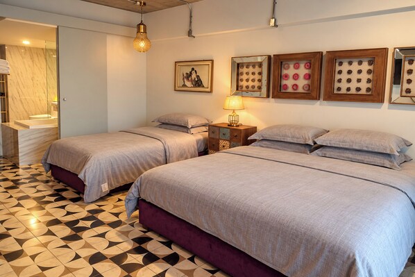 A hotel room with two beds, a bathroom, and a patterned floor. - River Art Hotel (Chiang Mai)