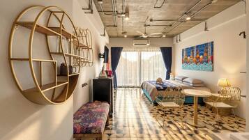 Habitació d'hotel moderna amb un sòl de disseny geomètric, una prestatgeria circular gran, un llit amb un capçal colorit, una taula rodona petita amb una làmpada i un quadre penjat a la paret.